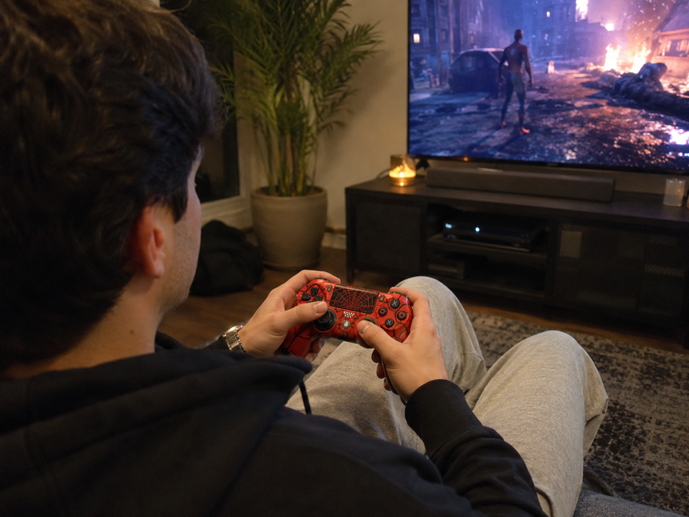 گیمر در حال استفاده از دسته بازی طرح دسته بازی PS4 قرمز SpiderMan در محیط خانگی